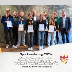 Mehrere Personen tragen jeweils eine Medaille um den Hals, eine Urkunde in den Händen und lächeln in die Kamera
