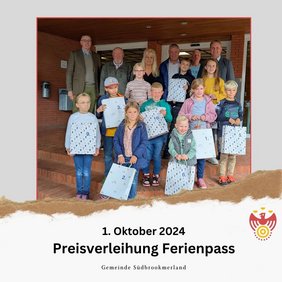 Preisverleihung Ferienpass. Einige Erwachsene und Kinder lächeln in die Kamera. Die Kinder halten jeweils eine Tüte.