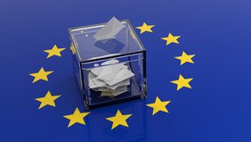 Eine durchsichtige Wahlurne auf blauem Grund mit gelben Sternen