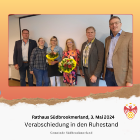 Mehrere Personen lächeln in die Kamera. Zwei Personen halten jeweils einen Blumenstrauß